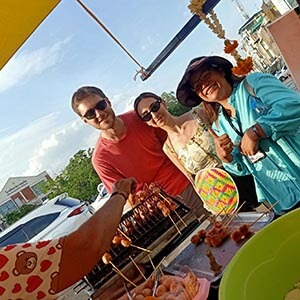 Guide Waza with Jeremy L. at a bustling Bangkok food market, smiling near colorful stalls filled with local produce and street food. 