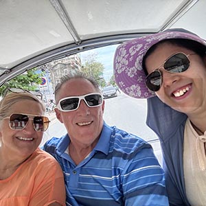 Guide Kung with Rebecca C. beside a colorful tuk-tuk in Bangkok, smiling with street views and local traffic in the background. 