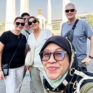 Guide UR with Wendy S. at Bangkok’s Victory Monument, smiling with the obelisk and traffic circle in the background.
