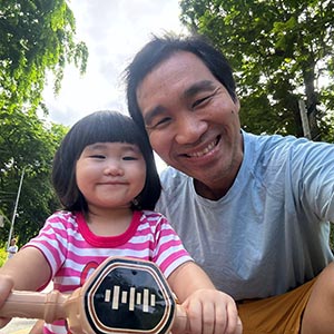 Nae, a tour guide, smiling outdoors in a light shirt, with his young daughter before work.