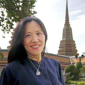 Kanny, a tour guide, smiling in a light‑colored top with a lanyard, standing outdoors with Bangkok temple architecture visible.