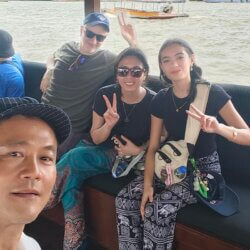 “Guide ChooChai with Lisa B. aboard a public ferry, smiling with river views and city structures in the background.
